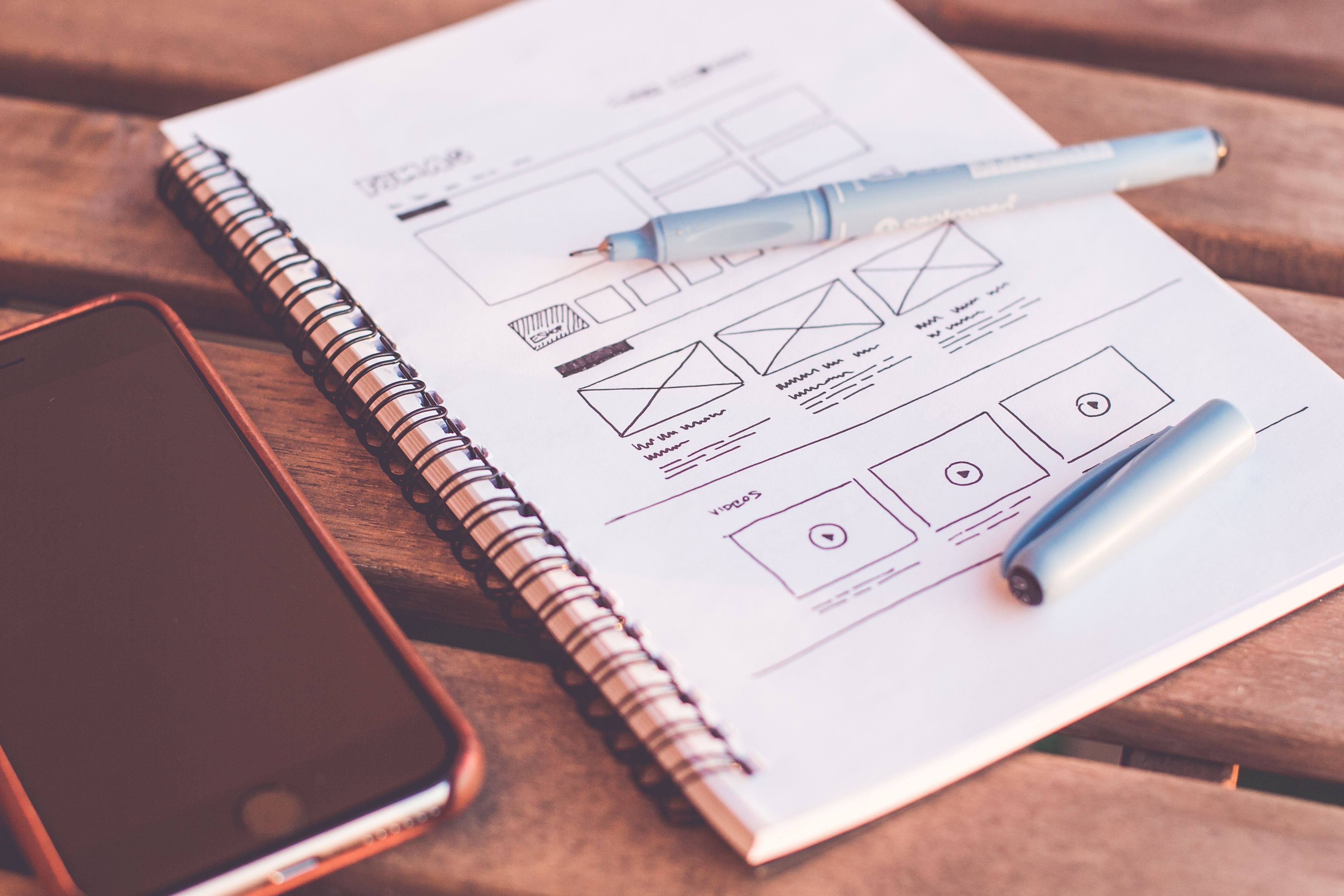 Hand-drawn website wireframes in a notebook beside a phone